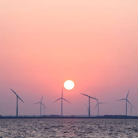 wind turbines and sun in colorful sky in the dutch province of flevoland