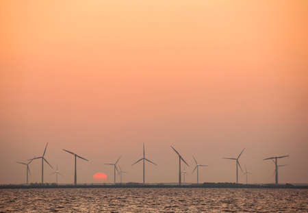wind turbines and rising sun in colorful sky in the dutch province of flevolandの写真素材