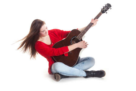 teenage girl sits and holds guitar in studio with white background