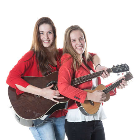 two teenage sisters have fun with ukelele and guitar in studio against white backgroundの写真素材