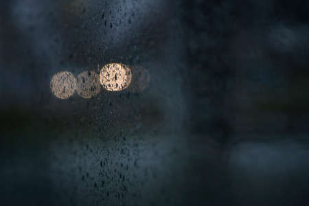 lights of traffic seen through wet windshield during rainfall in darknessの写真素材
