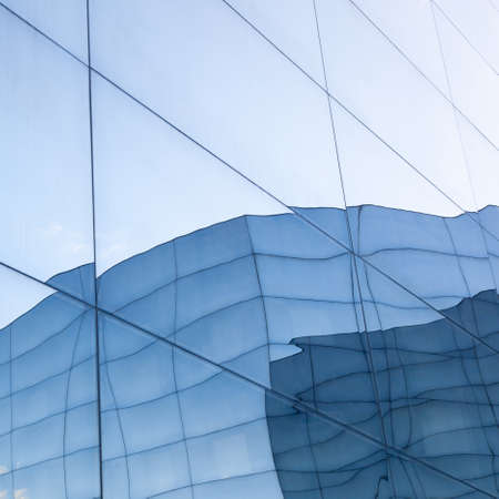 part of geometrically shaped modern glass building with reflections of blue sky and glass wall