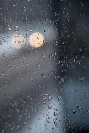 headlights of car in the dark seen through glass with raindropsの写真素材