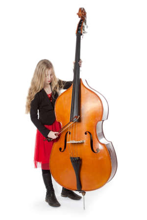 young blond girl in red dress plays double bass in studio against white backgroundの写真素材