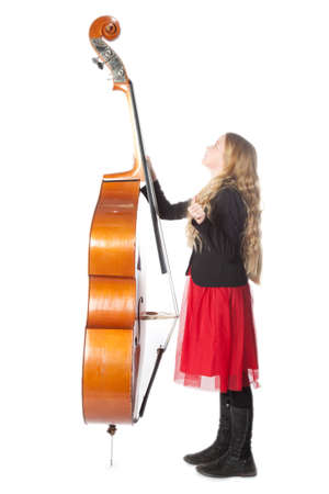 young blond girl in red dress looks up to double bass in studio against white background