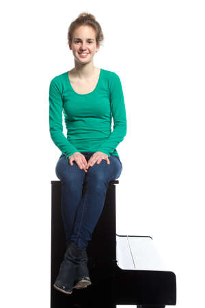 teenage girl sits on piano in green shirt and smilesの写真素材