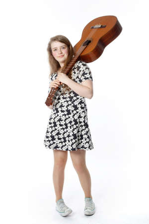 smiling teenage girl in dress holds guitar on shoulder in studio with white background