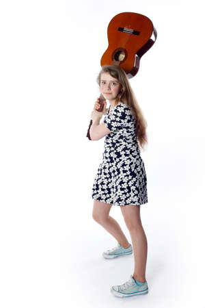 teenage girl in dress swings guitar in studio with white backgroundの写真素材