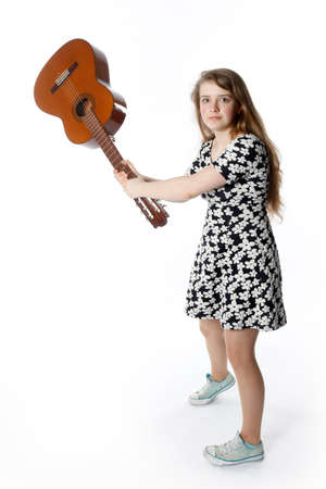 teenage girl in dress swings guitar in studio with white backgroundの写真素材