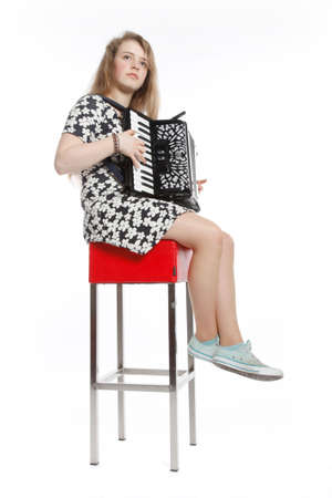 teenage girl sits on red stool in studio with accordion against white backgroyundの写真素材