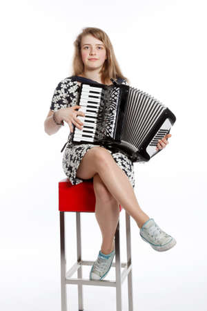 teenage girl sits on red stool in studio with accordion against white backgroundの写真素材