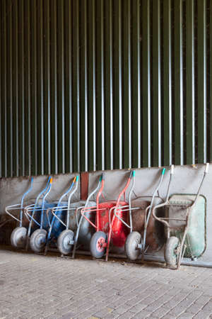 Six old and rusty wheelbarrows rest against wall of farm barnの写真素材