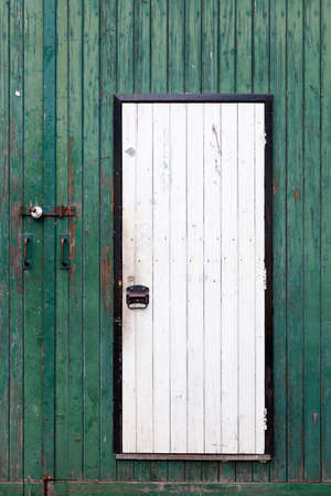 small white door in large green barn door with peeling green paintの写真素材