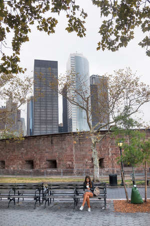 girl with mobile phone on bench near castle clinton in battery park downtown manhattanのeditorial素材