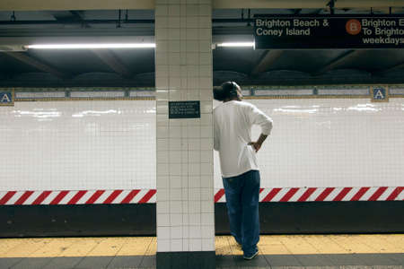 new york city, 11 september 2015: male african american waits on platform of subway and leans...