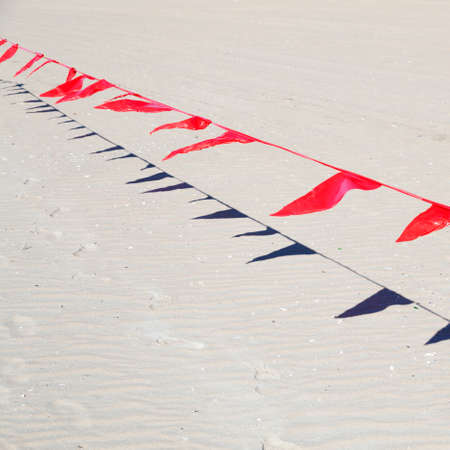 small red flags in wind against sand of beachの写真素材