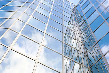 glass and steel office facade reflects clouds and blue skyの写真素材