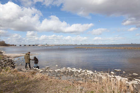 mother and child on stony shore and cloudscape above lake Gooimeer in the netherlands with Hollandse brug in the backgroundの写真素材
