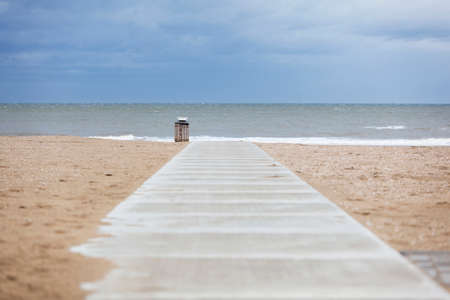 concrete path on deserted north sea beach with garbage can and cloudy skyの写真素材
