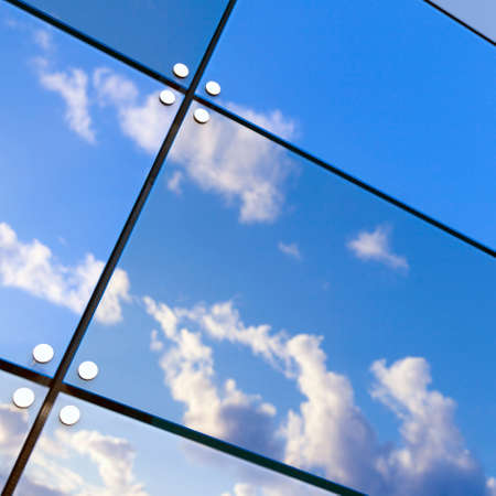 blue sky and white clouds reflect in glass panes of modern buildingの写真素材