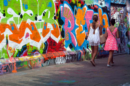 girls walk along walls full of grafiti in Belgian town of Ghent on sunny summer dayのeditorial素材