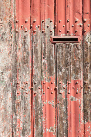 vertical part of old wooden door with letter box and bladdered red paint in sunshineの写真素材