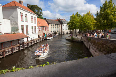 tourist boat in bruges canal near antique bridge on sunny summer day in augustのeditorial素材