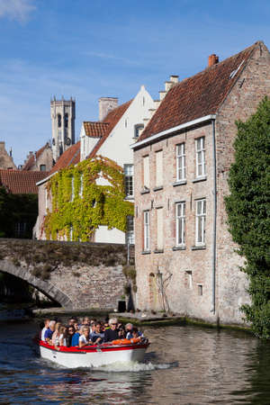 old houses and tourist boat in canal near bridge in centre of medieval Brugge in Belgium with blue sky in summerのeditorial素材