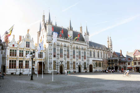 city hall of belgian town bruges in flanders on sunny summer morning with people biking and walkingのeditorial素材
