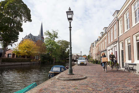 couple on bicycle passes houses along river Vecht in the dutch village of Maarssen in the netherlandsのeditorial素材