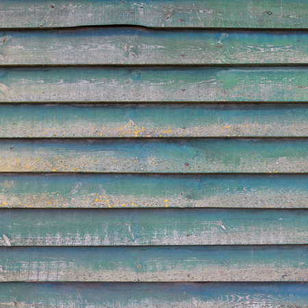 square part of shed wall consisting of old horizontal wooden planks with faded green paint and yellow mossの写真素材