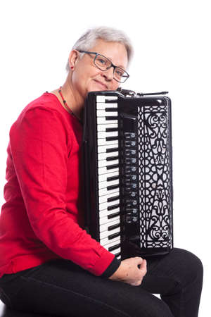 older caucasian woman with glasses plays accordion in studio with white backgroundの写真素材