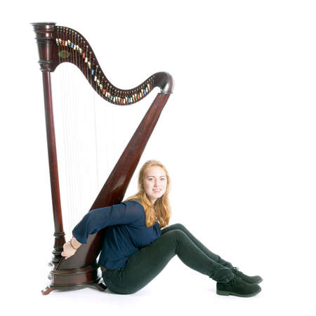 red blond caucasian teenage girl with harp sits on floor against white studio backgroundの写真素材