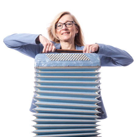 blond woman in blue with glasses holds accordeon and smiles in studio with white backgroundの写真素材