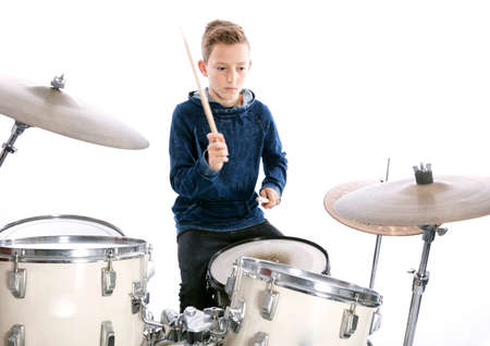 teenage boy behind drum kit in studio against white background