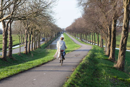 woman on bicycle descends dike to Purmer in dutch countryside north of amsterdamの写真素材