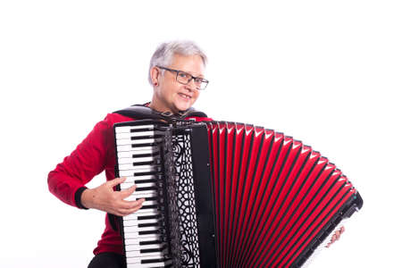older caucasian woman with glasses plays accordion in studio with white backgroundの写真素材