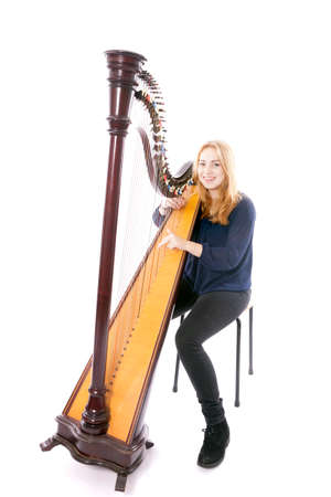red blond caucasian teenage girl plays the harp and smiles against white studio backgroundの写真素材
