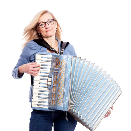 blond woman in blue with glasses plays the accordeon and smiles in studio with white backgroundの写真素材