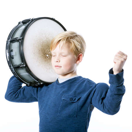 young blond boy with drum against white background in studio shows muscle and closed eyesの写真素材