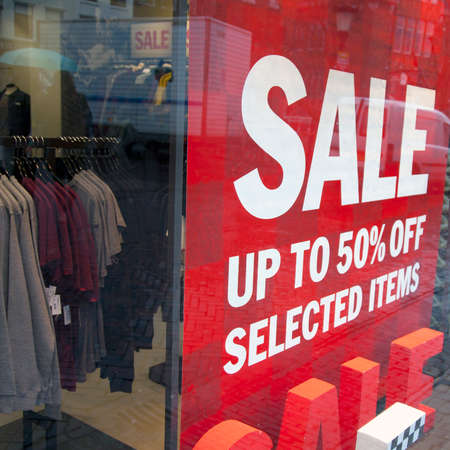 sale signs in display window of clothing store and sweaters and shirts in rack insideの写真素材