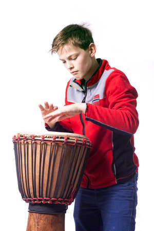 teenage caucasian boy plays the djembe in studio with white backgroundの写真素材