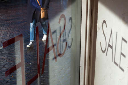 the word sale on shop window and woman with purse p[assing by on wet streetの写真素材