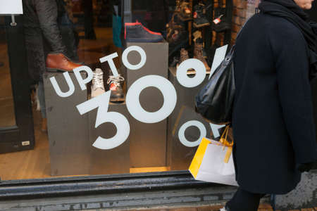 sale sign and discount numbers on shop window of shoe store and customer passing by