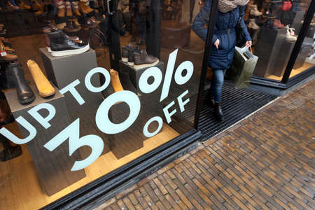sale sign and discount numbers on shop window of shoe store and customer leavingの写真素材