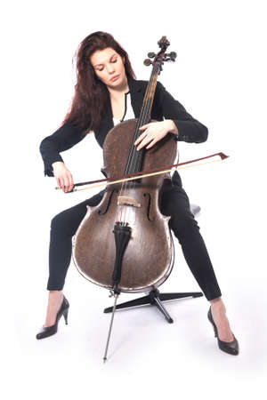 beautiful brunette woman in dark suit plays old brown violoncello in studio against white backgroundの写真素材