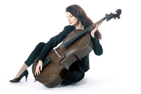 beautiful brunette woman sits on floor with old brown violoncello in studio against white backgroundの写真素材