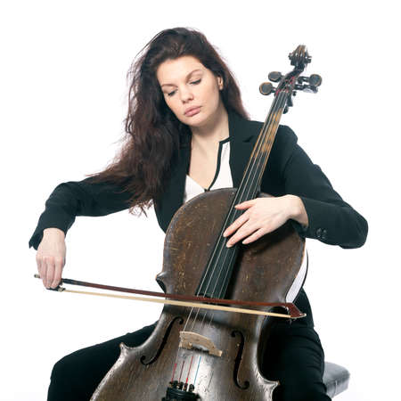 beautiful brunette woman plays old dark brown violoncello in studio against white backgroundの写真素材
