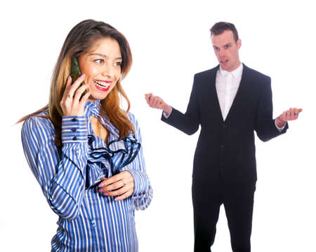 young woman talks into mobile phone while man in black suit looks not amusedの写真素材