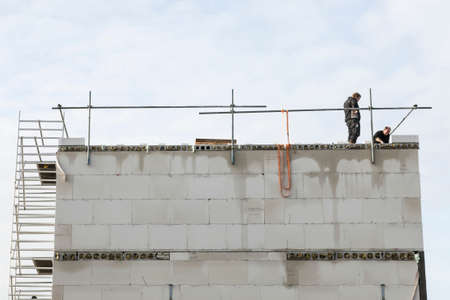 two workers on roof of new concrete house under construction with scaffolding and metal barsのeditorial素材